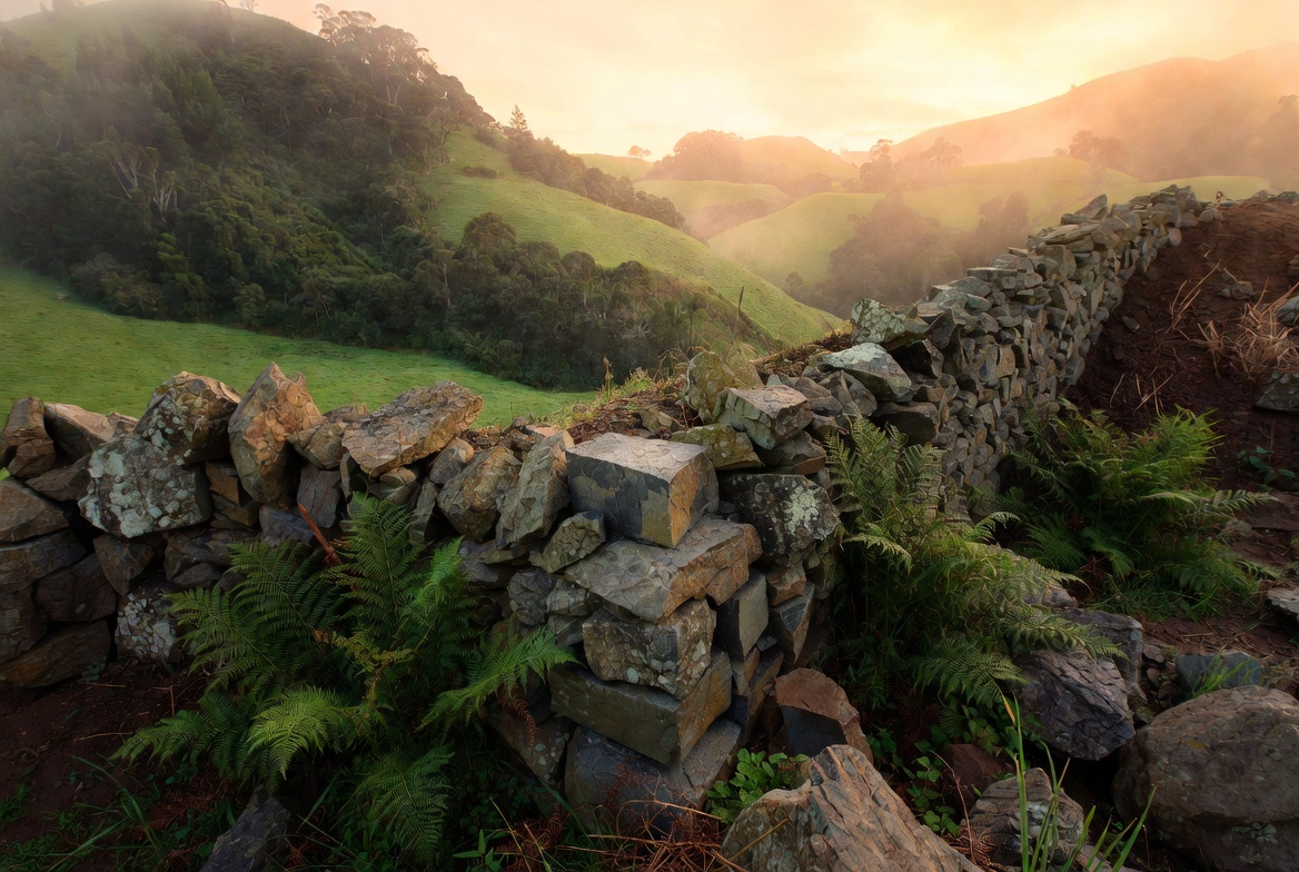 Stone wall foundation under construction in a green hillside